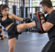 Woman practicing a controlled kickboxing drill with a coach in a modern MMA gym